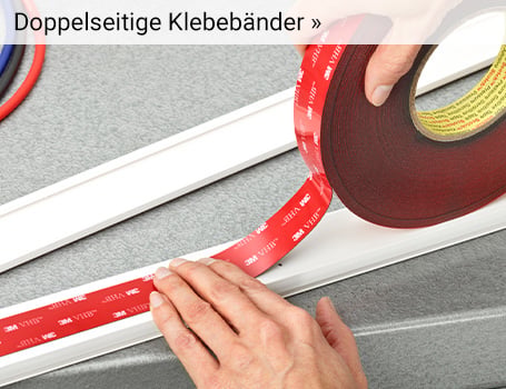  Das Bild zeigt aus der Nahansicht ein gewelltes, graues Material, das auf den Erhebungen mit einem roten, doppelseitigen Klebeband versehen ist, wobei im oberen linken Bereich eine Hand zu sehen ist, die das Material hält, und der Text "Doppelseitige Klebebänder »" im oberen Bereich des Bildes auf eine Weiterleitung hinweist.