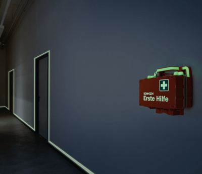 Eine leuchtende rote Söhngen Erste-Hilfe-Box hängt an einer dunklen Wand, umgeben von schwach leuchtenden Türrahmen.