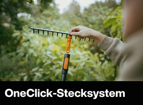 Eine Person montiert einen Rechen-Aufsatz auf einen schwarzen Stiel mit orangefarbenem Stecksystem vor einem grünen Hintergrund.