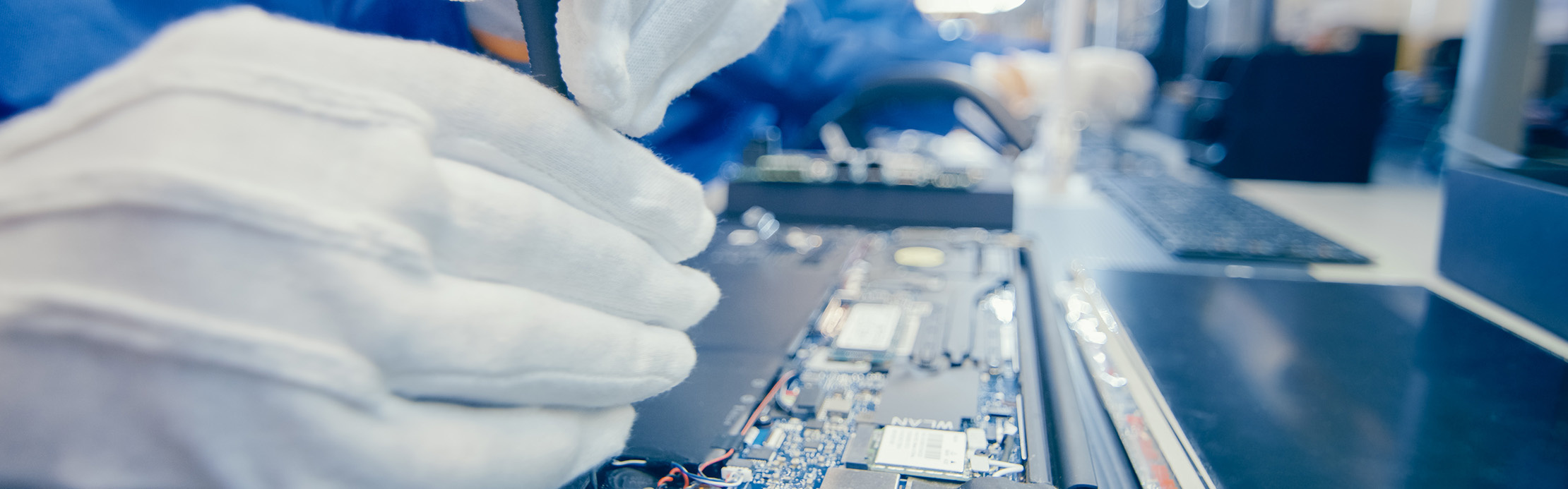 Person trägt Schutzhandschuhe und arbeitet mit einem Präzisionswerkzeug an einer geöffneten Leiterplatte für die Reparatur oder Wartung elektronischer Geräte.
