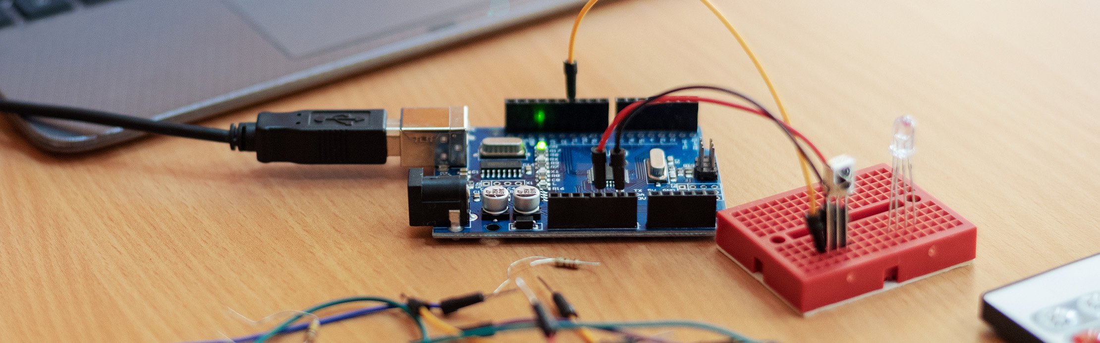 Arduino-Entwicklungsboard auf einem Schreibtisch, per USB verbunden und mit Kabeln an ein rotes Steckbrett mit LED angeschlossen.