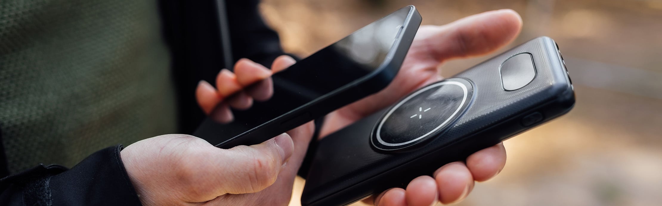 Person hält ein Smartphone und eine magnetische Powerbank in der Hand, um mobile Geräte unterwegs zuverlässig mit Energie zu versorgen.