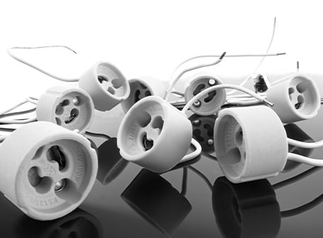  Eine Nahaufnahme in Graustufen zeigt eine Ansammlung von weißen, runden Lampensockeln, wahrscheinlich vom Typ GU5.3 oder GU10, mit angeschlossenen Kabeln, die als Zubehör für Beleuchtungssysteme dienen.