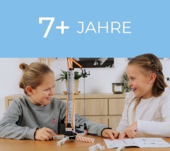 Ein hellblaues Banner mit dem Text "7+ JAHRE". Darunter sitzen ein Junge und ein Mädchen an einem Tisch und bauen mit fischertechnik.