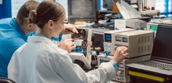 Zwei Personen arbeiten im Labor an Elektronik, eine Frau justiert ein Netzteil während der Messung.