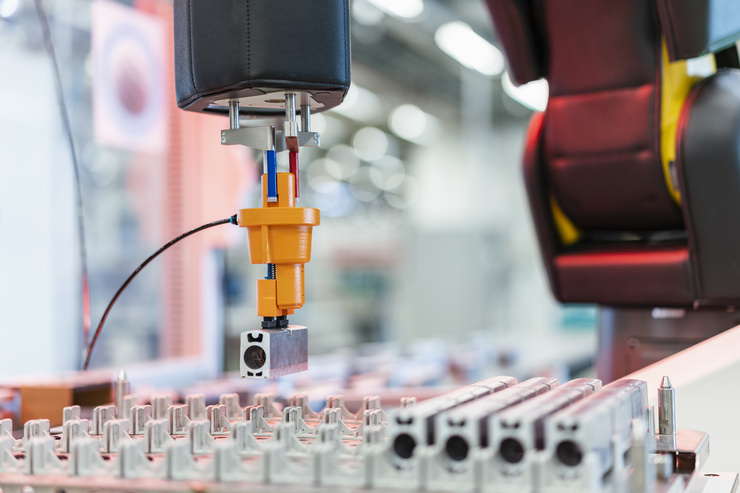 Ein Roboterarm hebt ein metallisches Bauteil in einer industriellen Produktionslinie an.