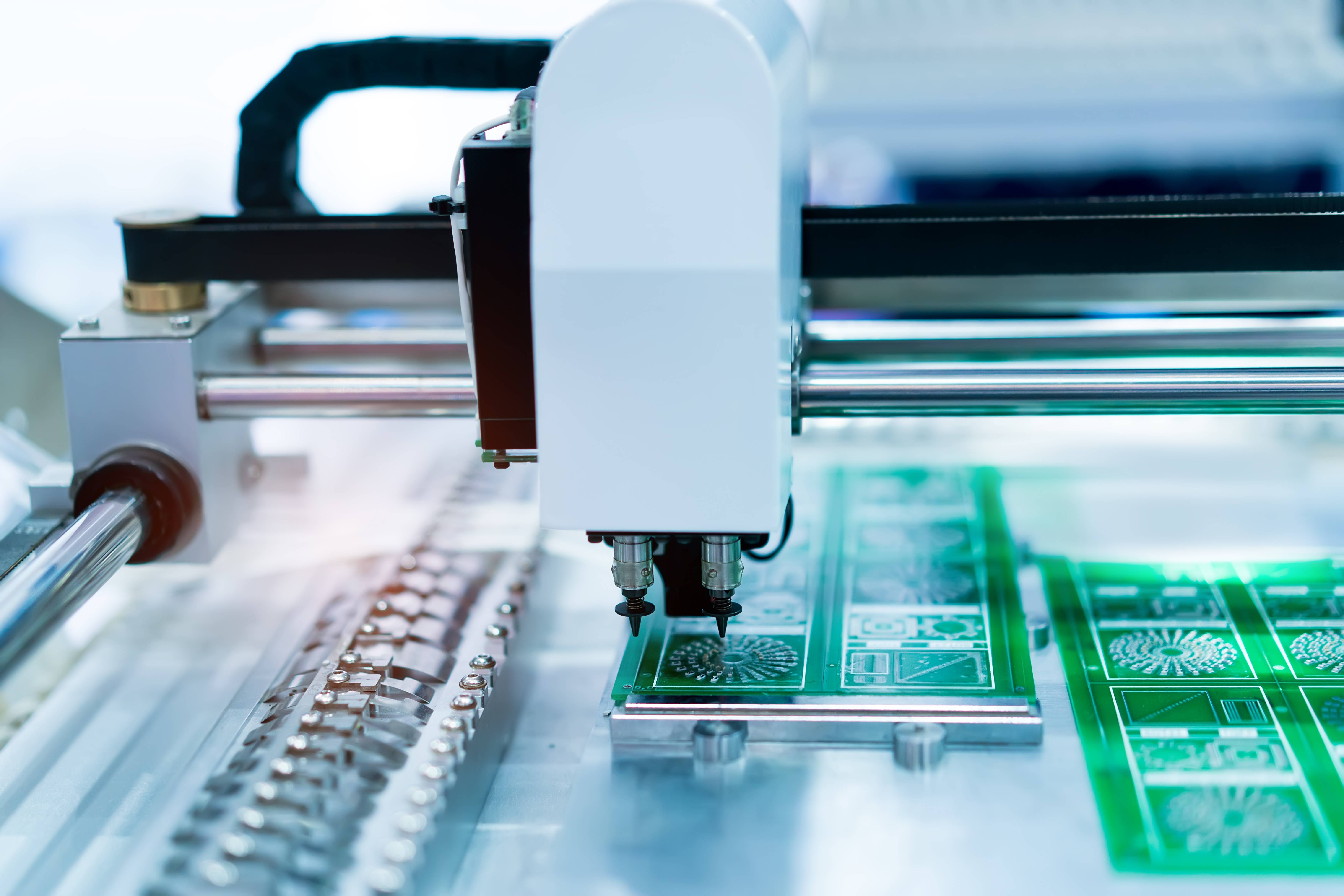 Eine Pick-and-Place-Maschine, die elektronische Bauteile auf grüne Leiterplatten montiert. Der Fokus liegt auf dem Präzisionsarm der Maschine.
