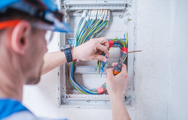 Elektriker arbeitet an einem offenen Verteilerkasten mit bunten Kabeln.