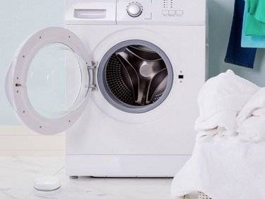 Weiße Frontlader-Waschmaschine mit offener Tür und Wäschekorb voller sauberer Wäsche.