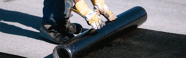 Ein Arbeiter auf dem Dach der Dichtungsmaterial ausrollt um Wasserschäden zu verhindern.