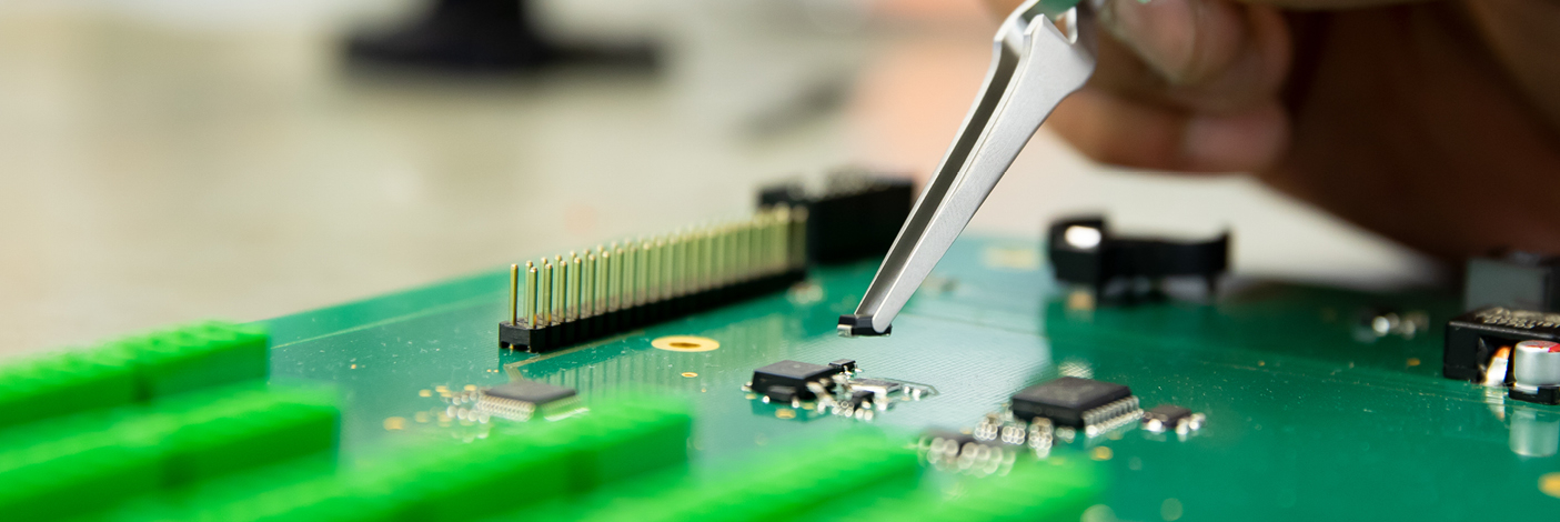 Iemand plaatst met een pincet een klein elektronisch onderdeel op een groene printplaat.