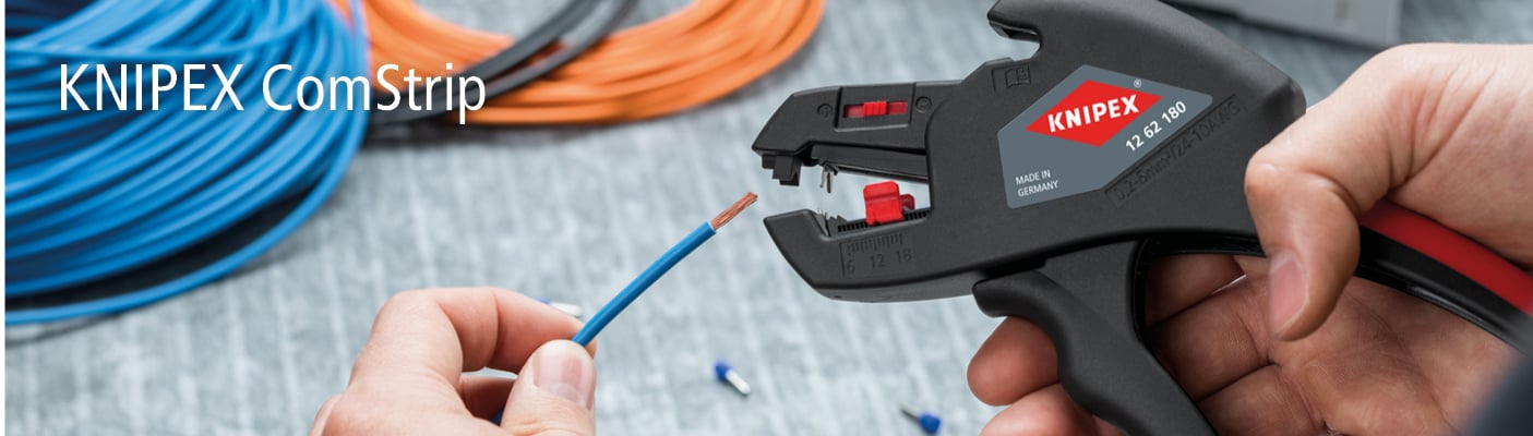 Eine Hand benutzt den Knipex ComStrip, ein schwarz-rotes Werkzeug, um die Isolierung eines blauen Drahtes abzuisolieren. Im Hintergrund liegen aufgerollte Kabel.