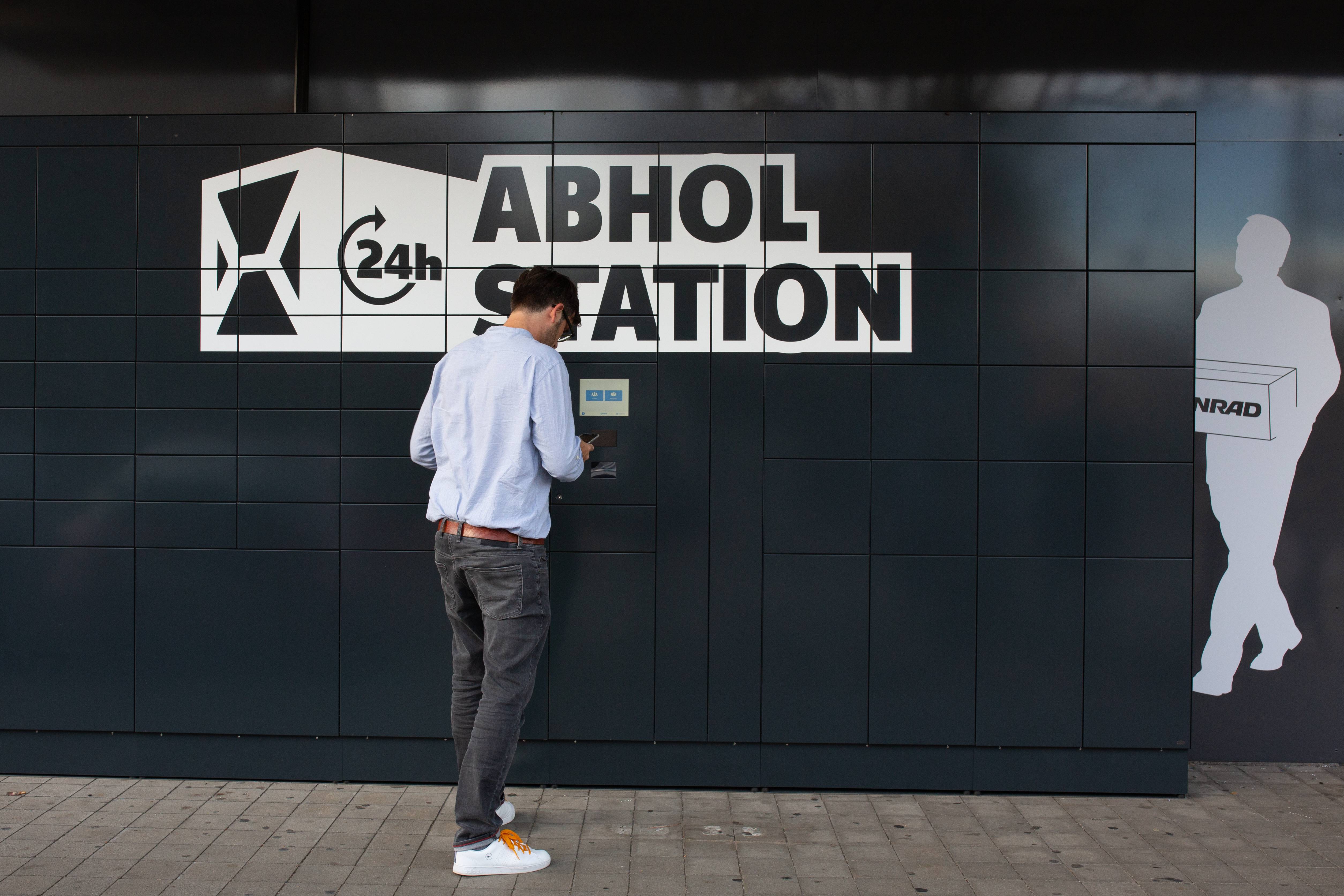 Mann mit Cap steht vor der Abholstation - diese ist schwarz mit weißer Aufschrift 24 Stunden Abholstation