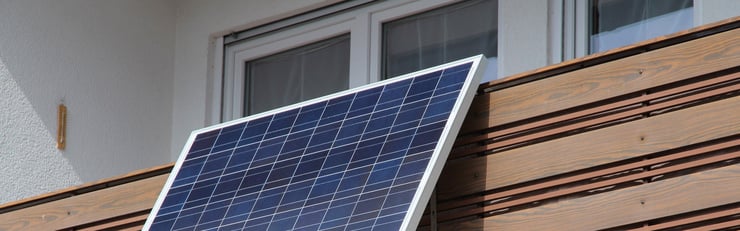 Solarmodul ist an einem Balkon vor einem Fenster befestigt und zur Sonne ausgerichtet.