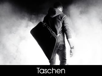 Eine stimmungsvolle Schwarz-Weiß-Rückansicht eines Mannes im Kapuzenpullover, der eine längliche Stativtasche an einem Schultergurt durch dichten Nebel trägt.