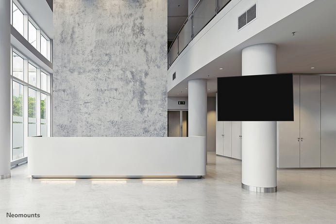 Das Bild einer modernen, minimalistischen Lobby zeigt einen weißen Empfangstresen, eine strukturierte Wand und einen großen Bildschirm.