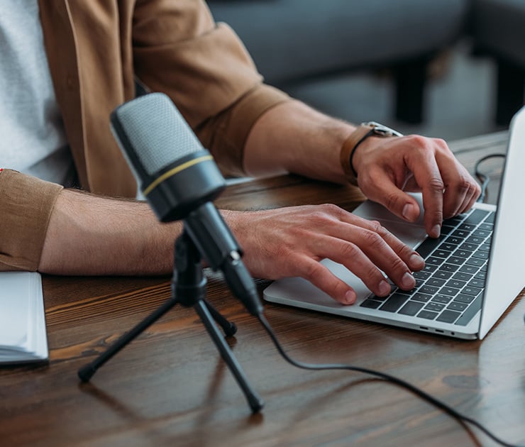 Eine Person tippt auf einem Laptop, während ein Mikrofon auf dem Tisch für Audioaufnahmen