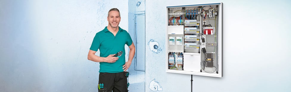 Un électricien se tient à côté d'un tableau électrique ouvert.