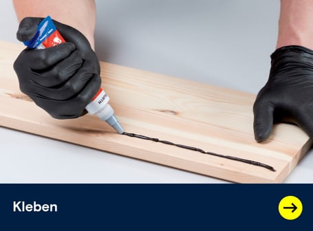  Dieses Teaserbild zeigt eine behandschuhte Hand, die einen schwarzen Klebstoffstreifen aus einer blauen Tube auf ein helles Holzbrett aufträgt, während im unteren Bereich des Bildes ein dunkelblaues Feld mit dem weißen Wort "Kleben" und einer Weiterleitung mit gelben Pfeil nach rechts.