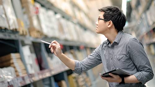 ein Mann steht im Lager, prüft den Lagerbestand und hat ein Tablet und einen Stift in der Hand