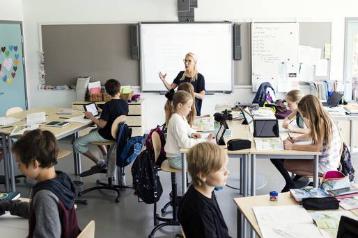 Eine Lehrerin hält Unterricht für eine Gruppe Schüler in einem modernen Klassenzimmer, viele nutzen Tablets.