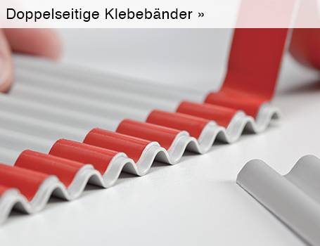  Das Bild zeigt aus der Nahansicht ein gewelltes, graues Material, das auf den Erhebungen mit einem roten, doppelseitigen Klebeband versehen ist, wobei im oberen linken Bereich eine Hand zu sehen ist, die das Material hält, und der Text "Doppelseitige Klebebänder »" im oberen Bereich des Bildes auf eine Weiterleitung hinweist.