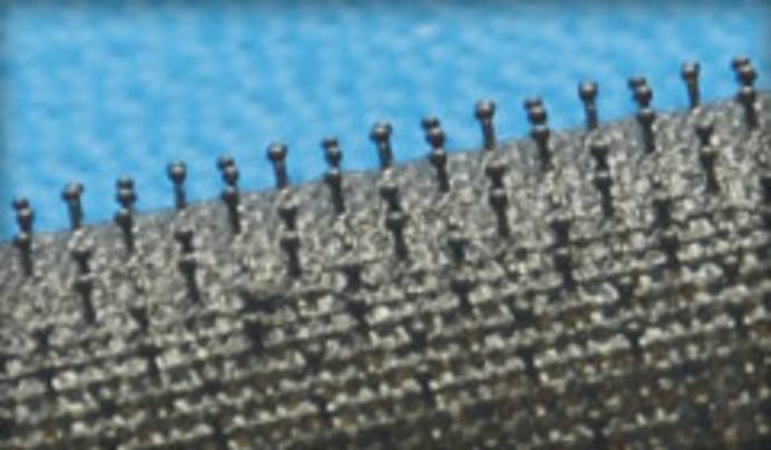 Detailansicht eines Pilzkopfbands. Zu sehen ist eine anthrazitfarbene Textilrolle, auf der in regelmäßigen Abständen kleine Noppen mit halbkugelförmigen Köpfen angeordnet sind.