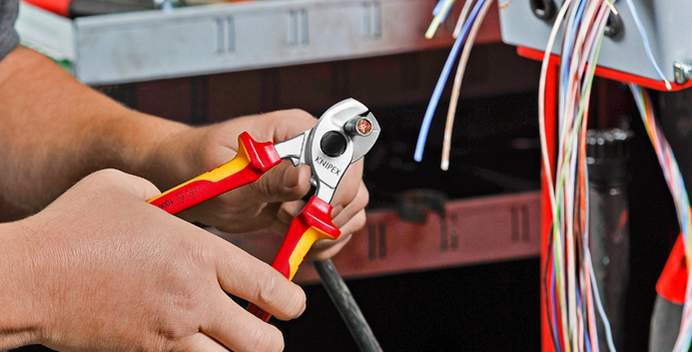 Een persoon knipt een kabel door met een tang met rood en geel handvat.