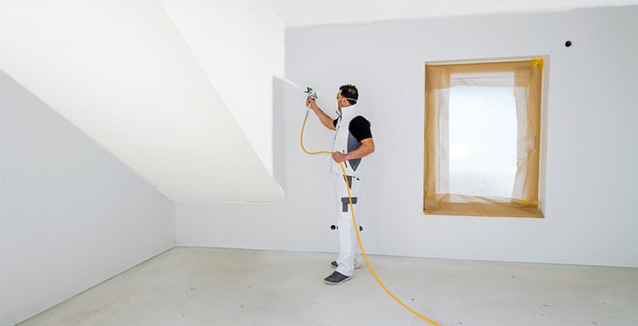 Ein Mann streicht eine Wand und Decke mit einem Wagner Sprühgerät PowerPainter 90 in einem leeren Raum.
