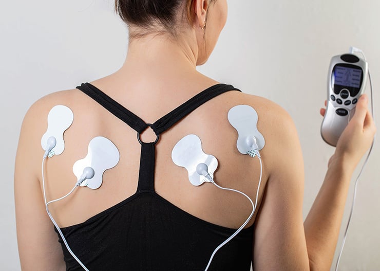 Person mit aufgeklebten Elektroden auf dem Rücken, verbunden mit einem EMS- bzw. TENS-Gerät zur Muskelstimulation und Entspannung.