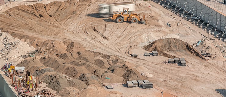 Grossbaustelle mit Radlader, Erdarbeiten und aufgeschütteten Sand- und Kieshaufen