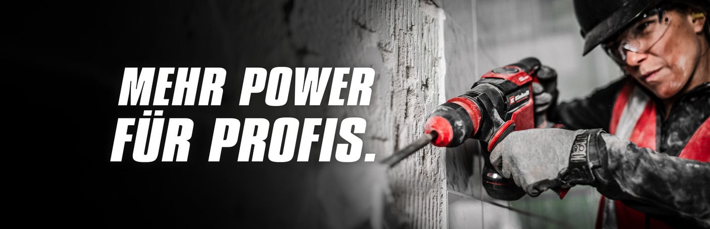  Ein professioneller Handwerker in Arbeitskleidung und Schutzbrille hält einen roten Einhell Akkuschrauber und schaut fokussiert nach vorne, während im Hintergrund ein Werkzeugregal zu erkennen ist.