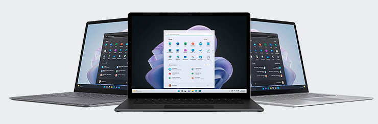 Drei Laptops in unterschiedlichen Farben mit geöffnetem Windows-Startmenü auf den Bildschirmen.