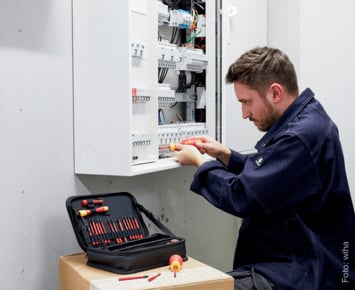 Das Bild zeigt einen Elektriker bei der Arbeit an einem Elektro-Installationskasten in einem Hausanschlussraum eines Gebäudes.