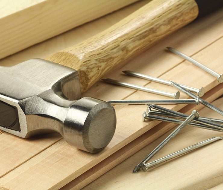 Hammer mit Holzgriff und mehrere Nägel liegen auf hellen Holzbrettplatten.