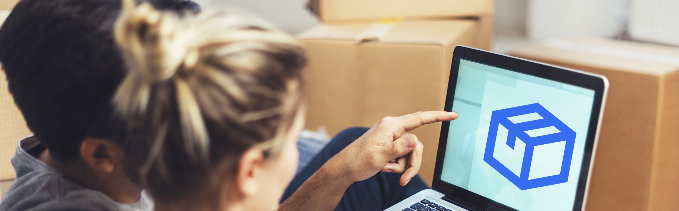 Zwei Personen schauen auf einen Laptop mit Paket-Symbol, im Hintergrund stehen Umzugskartons.