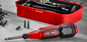  Ein roter, handgeführter Akkuschrauber mit einem grauen Griff und einer schwarzen Spitze, der vor einem offenen roten Werkzeugkoffer auf einem grauen Holztisch liegt, umgeben von verschiedenen Schrauben und Bit-Aufsätzen