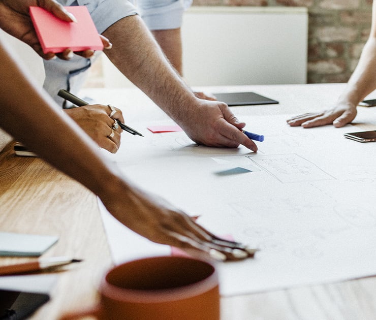 Mehrere Personen arbeiten gemeinsam an einem großen Papierbogen und schreiben Notizen darauf.
