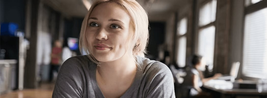 Dieses Bild zeigt eine moderne Büroumgebung mit mehreren Personen, die miteinander interagieren und arbeiten. Die Wand ist hell und kreativ mit einem abstrakten Muster gestaltet. Zentral in der Mitte des Bildes steht ein Multifunktionsdrucker mit mehreren Papierfächern. Pflanzen und natürliches Licht verbessern das Ambiente. Diese Umgebung wirkt entspannt und gleichzeitig produktiv, was die Zusammenarbeit und Kreativität fördert.