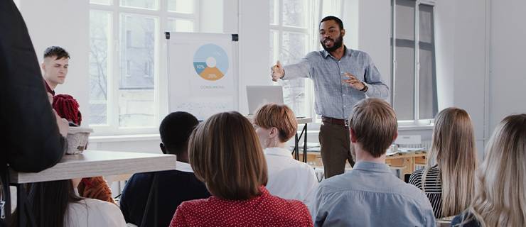 Mann präsentiert Geschäftsgrafiken auf Flipchart vor einer Gruppe im Seminarraum.