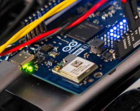 Nahaufnahme eines blauen Arduino Uno Mikrocontrollers mit angeschlossenen bunten Kabeln und leuchtenden Kontroll-LEDs.