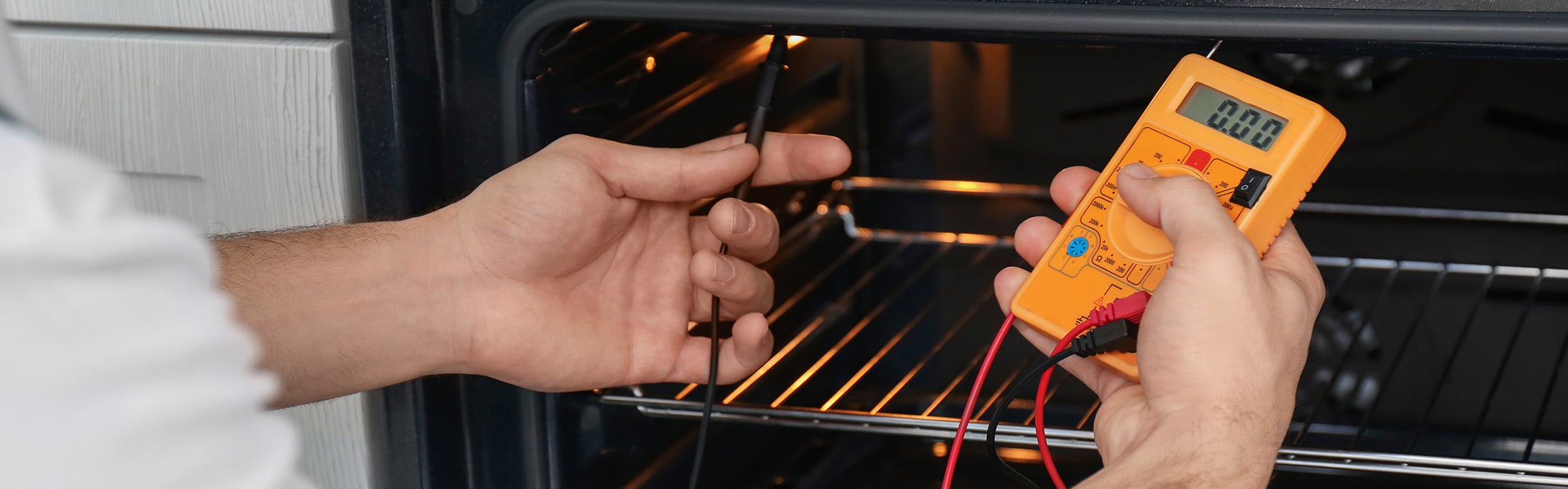 Person prüft einen Backofen mit einem digitalen Multimeter und einer Messsonde.