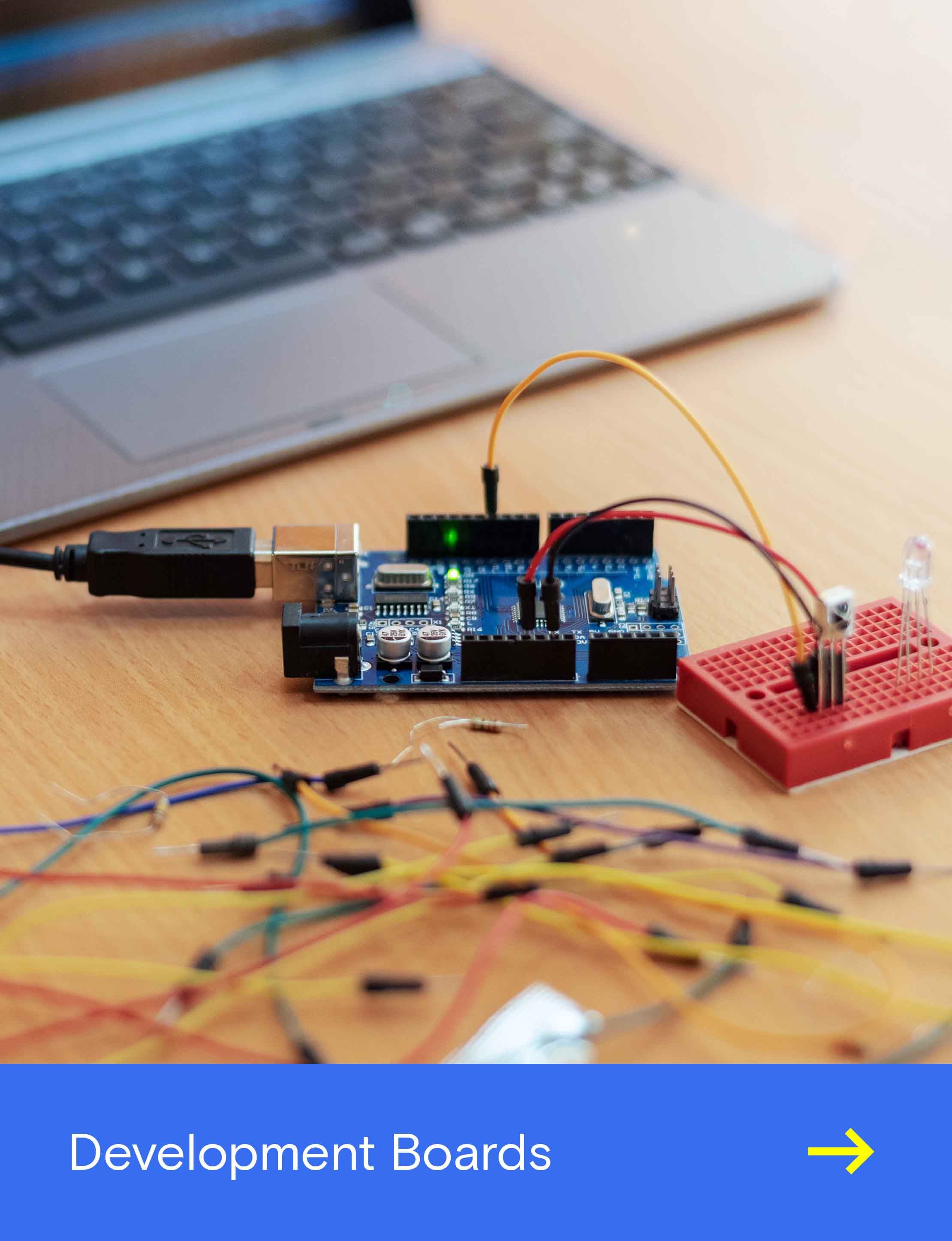 Arduino-Entwicklungsboard auf einem Schreibtisch, per USB verbunden und mit Kabeln an ein rotes Steckbrett mit LED angeschlossen.