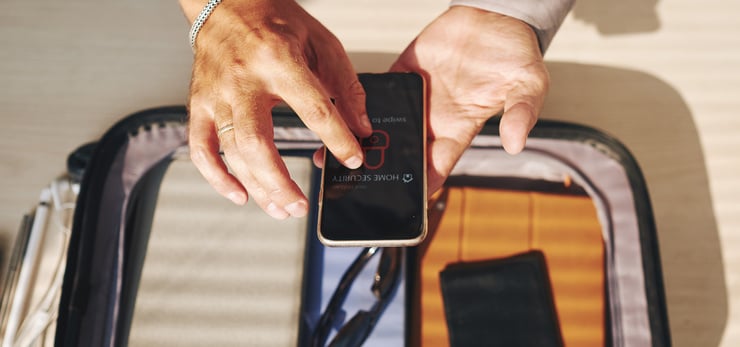 Person aktiviert eine Sicherheits-App auf dem Smartphone, während persönliche Wertgegenstände sicher in einer Tasche verstaut sind.