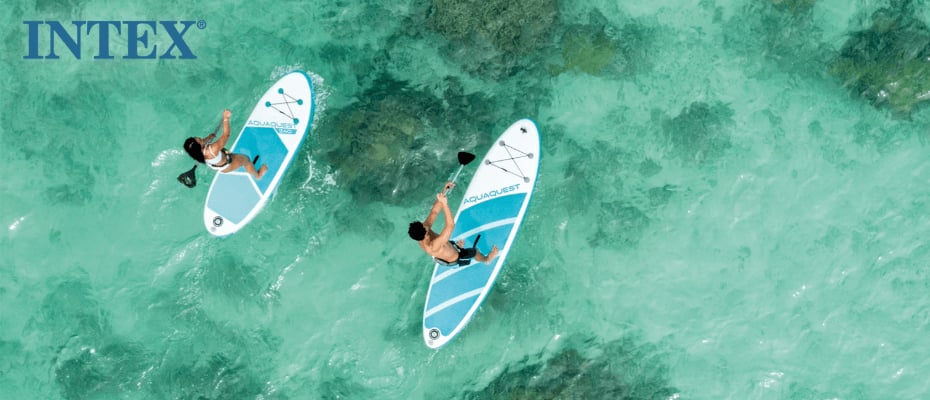 Im Bild sind zwei Personen zu sehen, die auf klarem, türkisfarbenem Wasser mit aufblasbaren Stand-Up-Paddleboards (SUPs) der Marke Intex paddeln. Die Szene ist ruhig und fängt die Essenz einer entspannten Wassersportaktivität in einer tropischen Umgebung ein.
