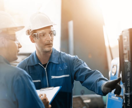 Das Bild zeigt zwei Arbeiter an einer Maschine in einer Industriehalle.