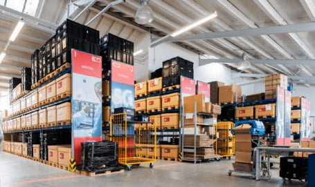Blick in eine gut strukturierte Lagerhalle mit hohen Regalen voller markierter Pakete und speziellen Sektionen für Medizintechnik und Telekommunikation.