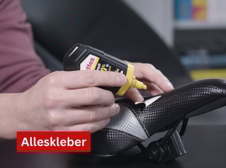 Eine Tube Alleskleber wird verwendet, um einen schwarzen Schuh zu kleben, wobei die Klebstoffspitze auf eine Naht gerichtet ist.