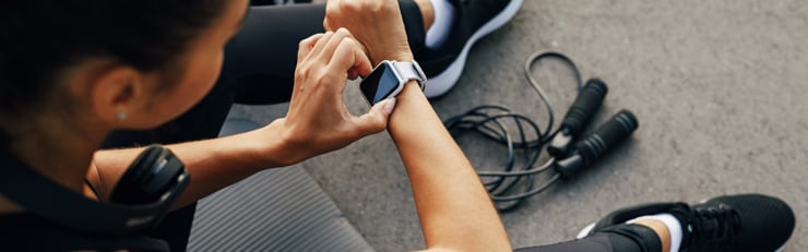 Person beim Training überprüft eine Smartwatch, Fitness-Tracker am Handgelenk, Springseil und Sportbekleidung – Aktivitäts- und Trainingskontrolle im Alltag.