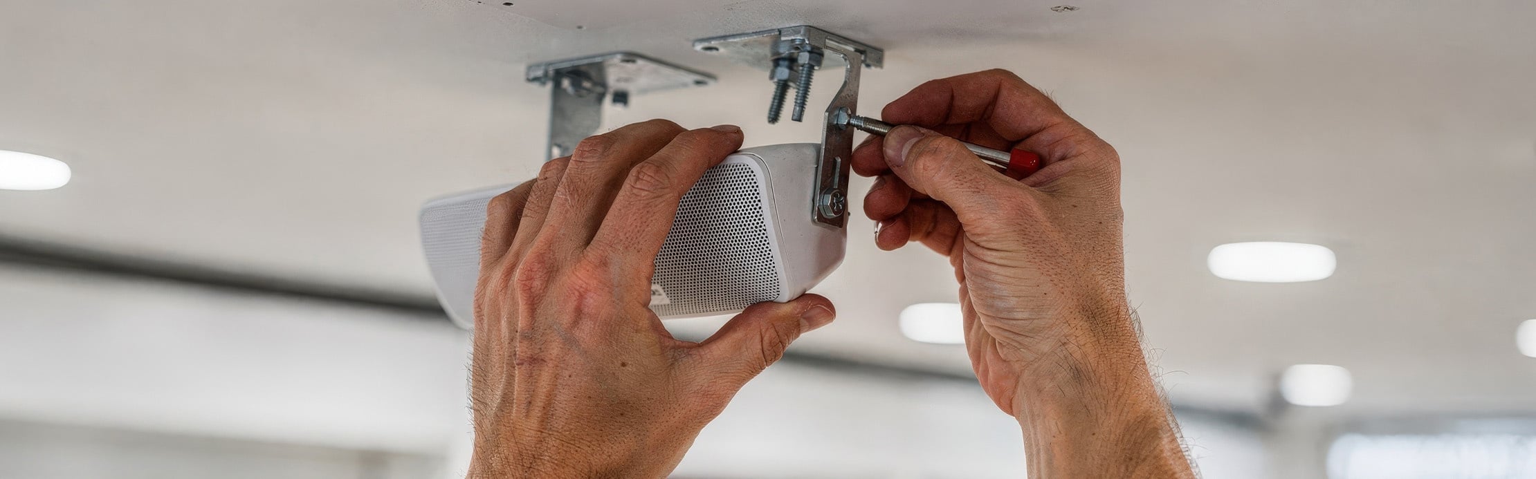 Person befestigt einen Lautsprecher mit einer Metallhalterung an der Decke